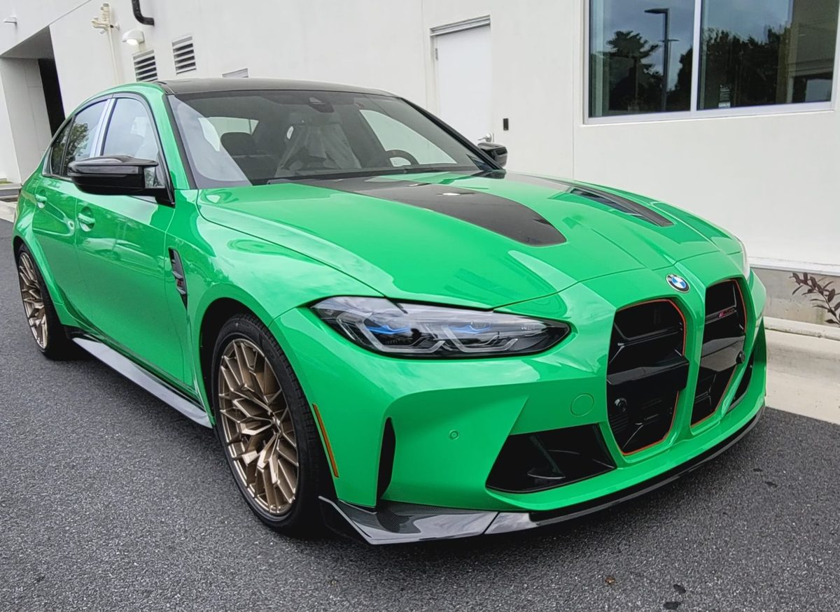 A green BMW M3 with bronze wheels and a carbon-fiber hood