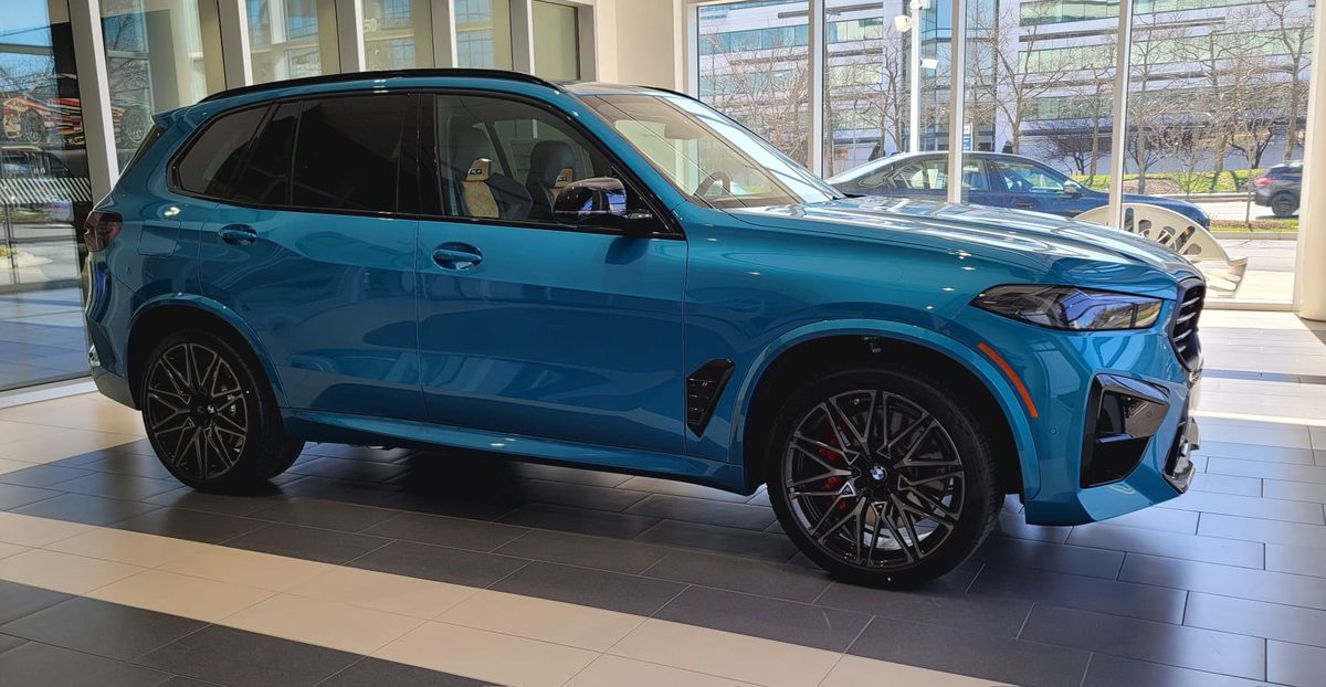 A current-generation BMW X5 M Competition in blue on a BMW showroom floor