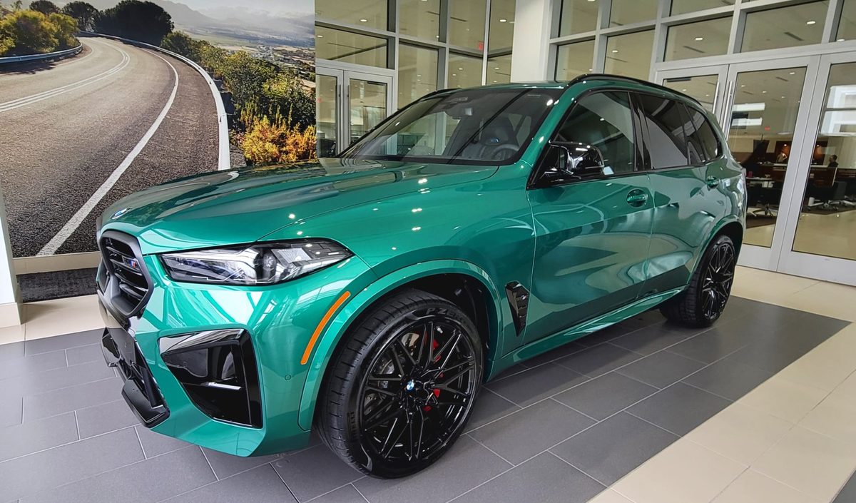 A current-generation BMW X5 M Competition in green on a BMW showroom floor